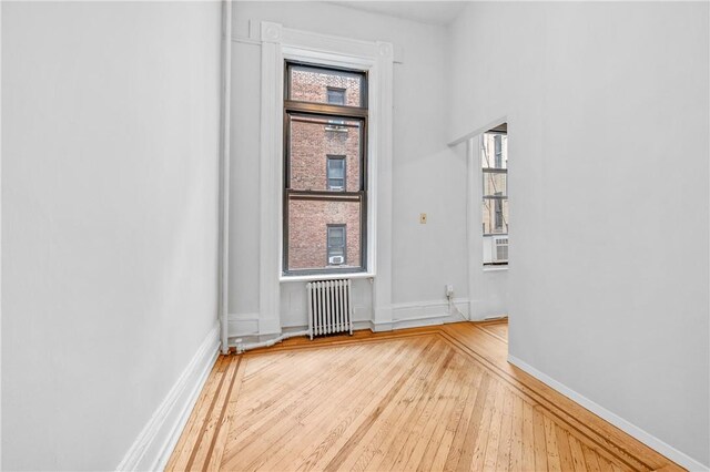 empty room with cooling unit, a healthy amount of sunlight, radiator, and light hardwood / wood-style flooring