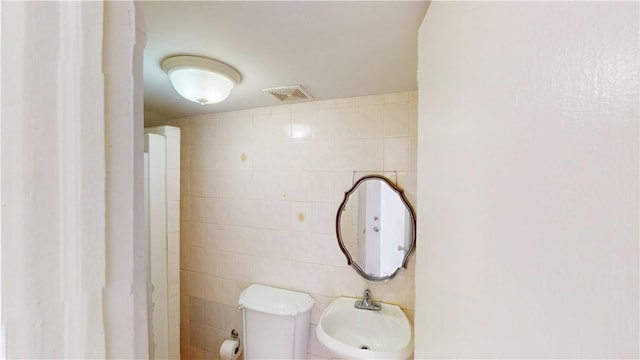 bathroom with toilet, tile walls, and sink