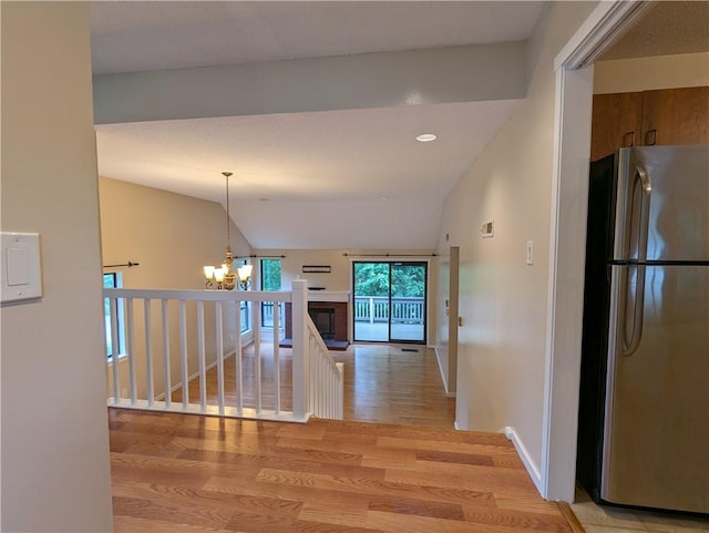 hall with light hardwood / wood-style flooring, lofted ceiling, and an inviting chandelier