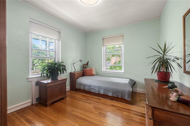 bedroom with light hardwood / wood-style floors, radiator heating unit, and multiple windows