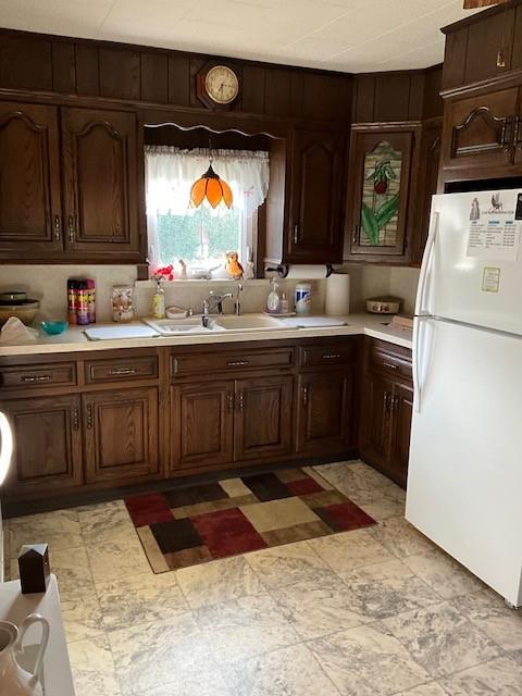 kitchen featuring dark brown cabinetry, white fridge, wooden walls, and sink