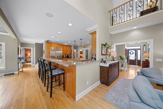 kitchen with kitchen peninsula, light wood-type flooring, light stone counters, decorative light fixtures, and stainless steel built in fridge