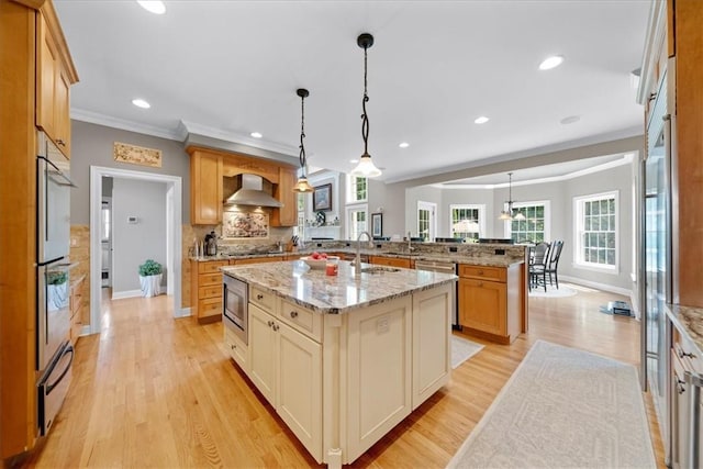 kitchen featuring light stone counters, wall chimney exhaust hood, pendant lighting, light hardwood / wood-style flooring, and an island with sink