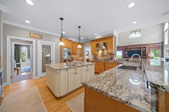 kitchen featuring a large island, sink, wall chimney exhaust hood, pendant lighting, and light wood-type flooring