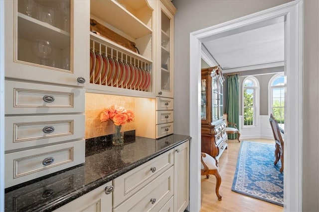 interior space featuring white cabinetry, dark stone countertops, light wood-type flooring, decorative backsplash, and ornamental molding