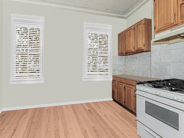 kitchen featuring decorative backsplash, crown molding, white range with gas stovetop, and light hardwood / wood-style floors