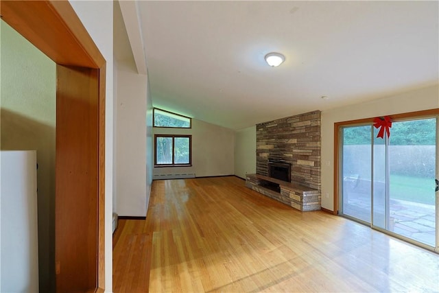 unfurnished living room with light hardwood / wood-style floors, lofted ceiling, a fireplace, and a baseboard heating unit