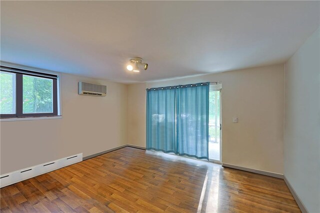 unfurnished room featuring baseboard heating, an AC wall unit, and hardwood / wood-style flooring