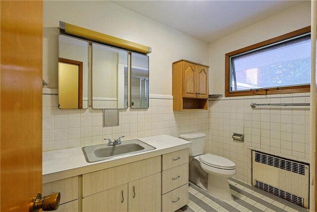 bathroom featuring tile patterned floors, vanity, tile walls, radiator heating unit, and toilet