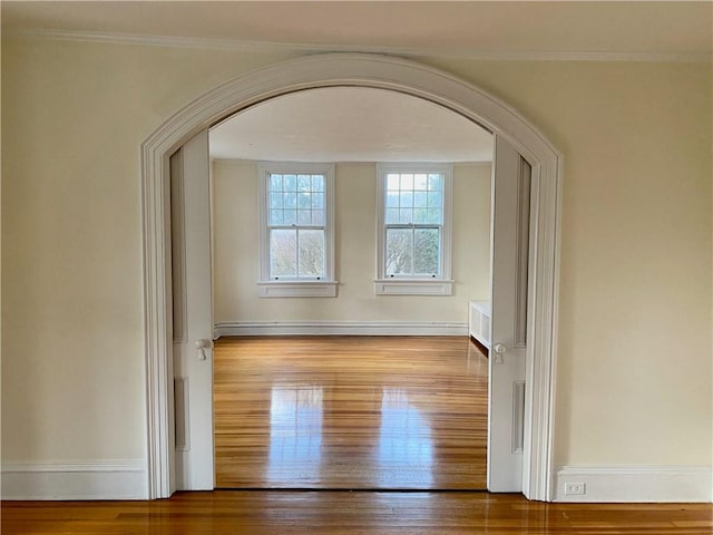 unfurnished room with wood-type flooring, a baseboard radiator, and ornamental molding