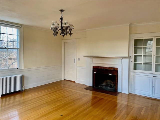 unfurnished living room featuring wood-type flooring, radiator heating unit, ornamental molding, and a chandelier