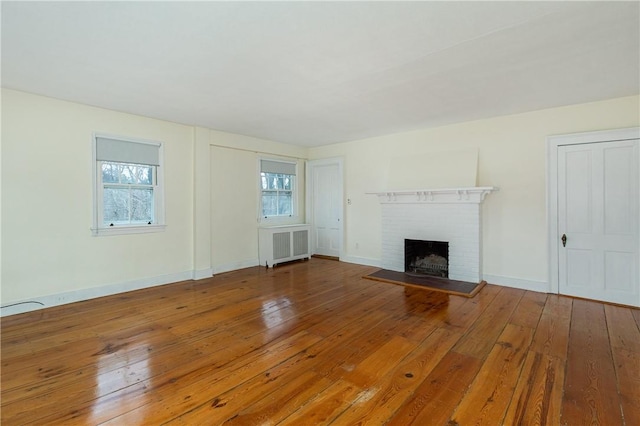 unfurnished living room featuring radiator heating unit, hardwood / wood-style flooring, and a brick fireplace