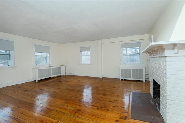 unfurnished living room with a fireplace, a wealth of natural light, radiator heating unit, and hardwood / wood-style floors