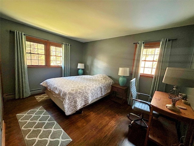 bedroom featuring multiple windows, dark hardwood / wood-style flooring, and a baseboard heating unit