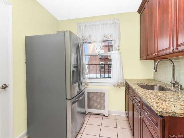 kitchen with light stone countertops, sink, radiator heating unit, stainless steel fridge, and light tile patterned floors