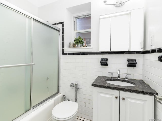 full bathroom featuring shower / bath combination with glass door, vanity, toilet, and tile walls