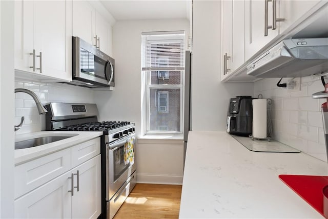 kitchen with backsplash, stainless steel appliances, sink, white cabinets, and light hardwood / wood-style floors