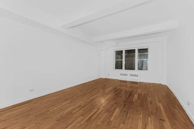 empty room featuring beamed ceiling, wood-type flooring, and radiator heating unit