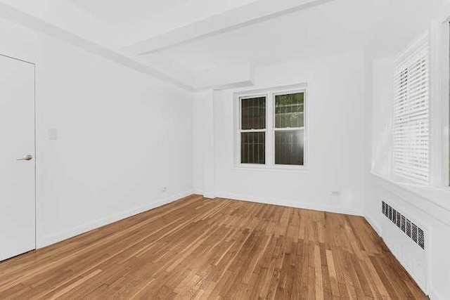 unfurnished room with beamed ceiling, radiator heating unit, and hardwood / wood-style floors