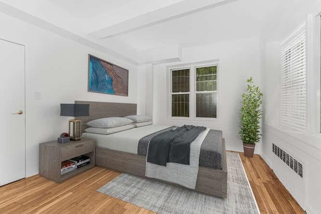 bedroom with hardwood / wood-style flooring, radiator heating unit, and multiple windows