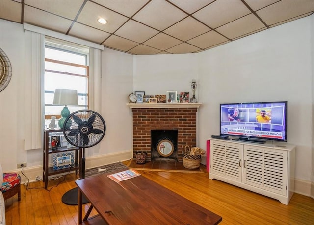 living room featuring hardwood / wood-style flooring, a brick fireplace, and a drop ceiling