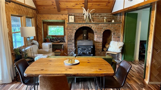 dining space with vaulted ceiling with beams, hardwood / wood-style flooring, a wood stove, and wood walls