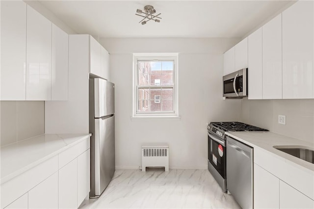 kitchen with white cabinets, appliances with stainless steel finishes, light stone countertops, and radiator