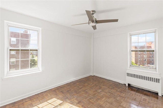 empty room with ceiling fan, a healthy amount of sunlight, dark parquet flooring, and radiator heating unit