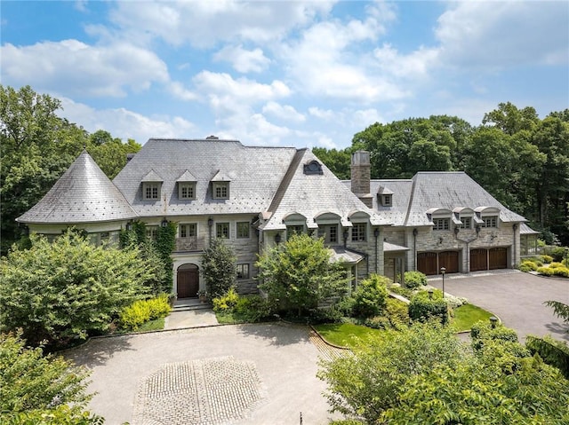 view of front of house with a high end roof, a chimney, driveway, and stone siding