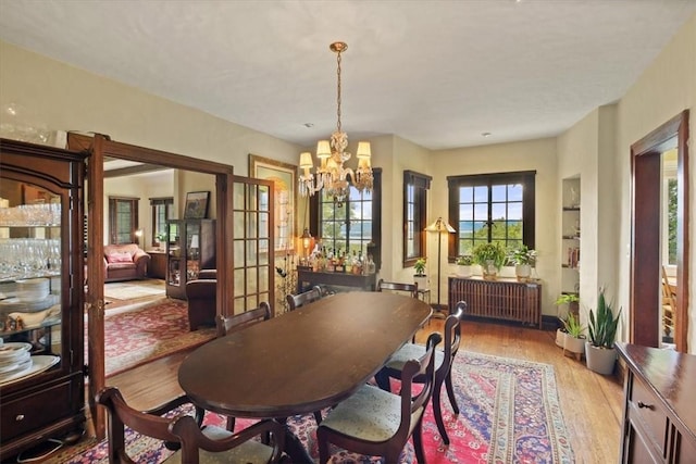 dining area with light wood-type flooring, radiator, and an inviting chandelier