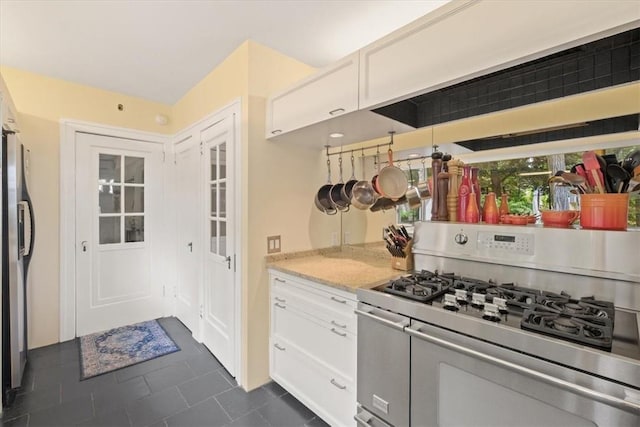 kitchen with white cabinets, stainless steel appliances, light stone counters, and dark tile patterned floors