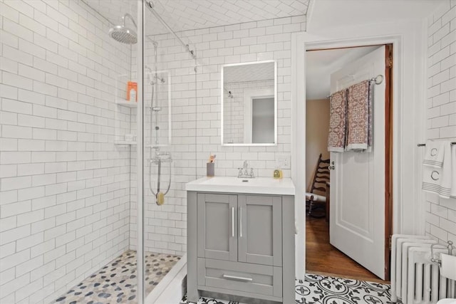 bathroom with tile patterned flooring, a shower with shower door, radiator heating unit, and vanity