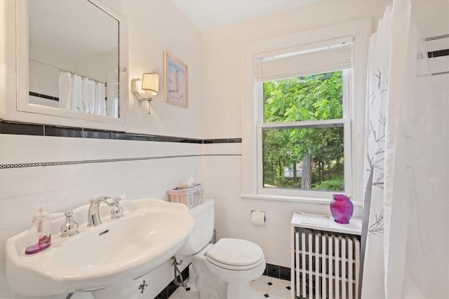 bathroom with toilet, sink, radiator, and tile walls