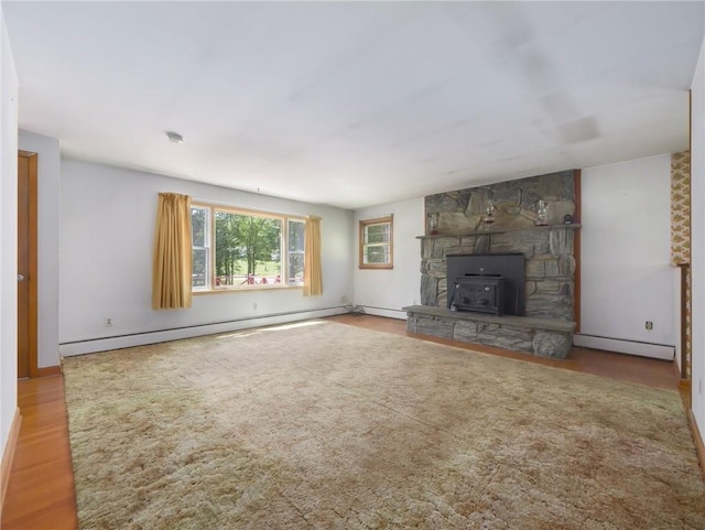 unfurnished living room with wood-type flooring, a wood stove, and a baseboard heating unit