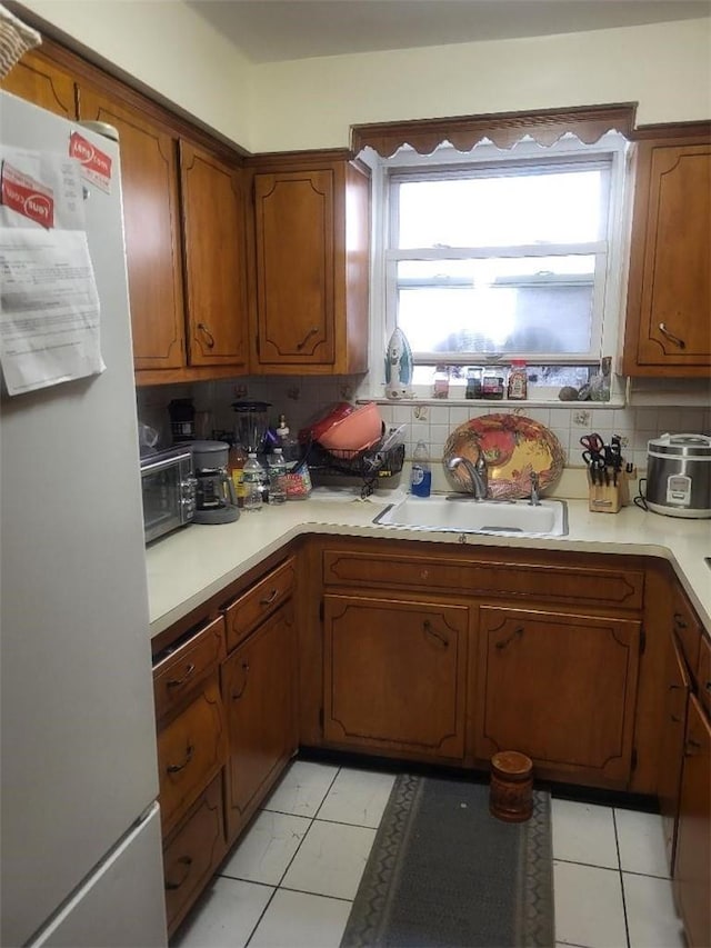 kitchen featuring white fridge, light tile patterned floors, sink, and tasteful backsplash