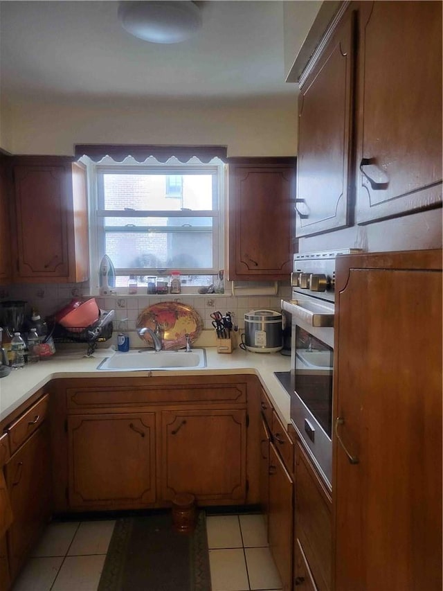 kitchen featuring decorative backsplash, stainless steel oven, light tile patterned flooring, and sink