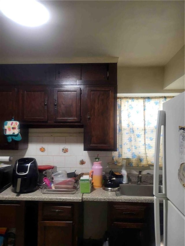 kitchen featuring dark brown cabinets, white refrigerator, sink, and backsplash