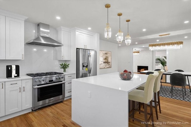 kitchen with wall chimney exhaust hood, light wood-type flooring, white cabinetry, and appliances with stainless steel finishes