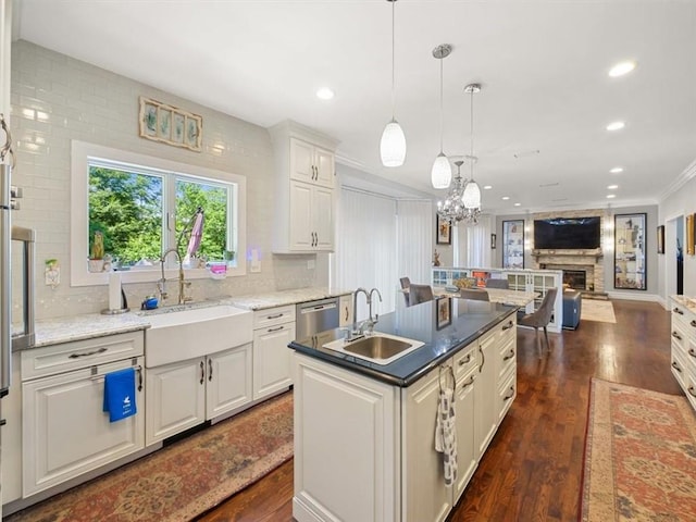 kitchen with dark wood-type flooring, sink, ornamental molding, a fireplace, and an island with sink