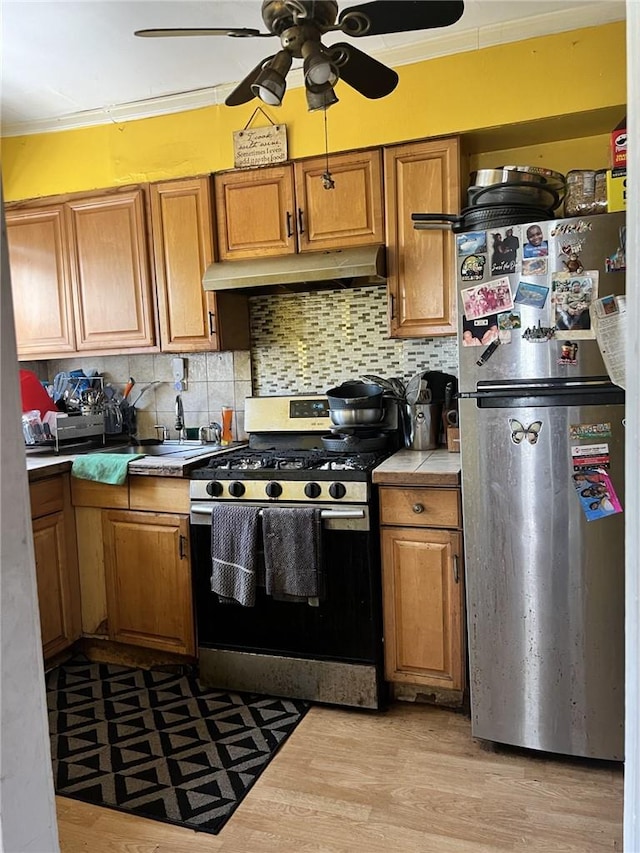 kitchen with tile counters, tasteful backsplash, crown molding, appliances with stainless steel finishes, and light wood-type flooring