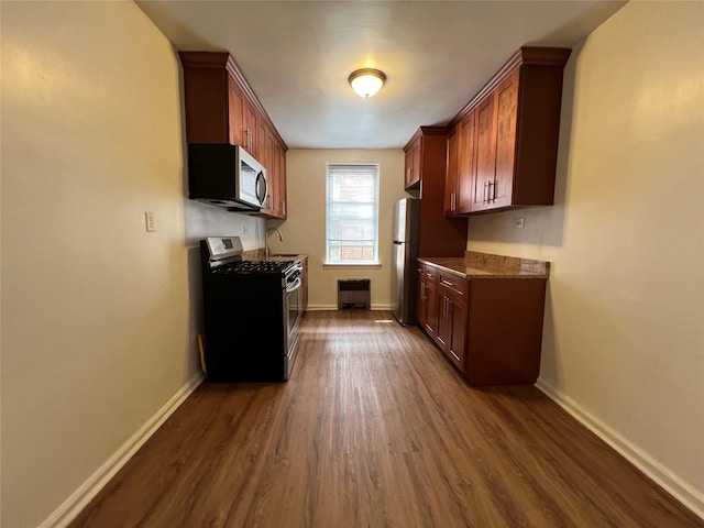 kitchen with appliances with stainless steel finishes, dark hardwood / wood-style floors, and radiator heating unit