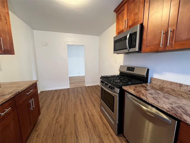 kitchen with dark wood-type flooring, light stone countertops, and appliances with stainless steel finishes