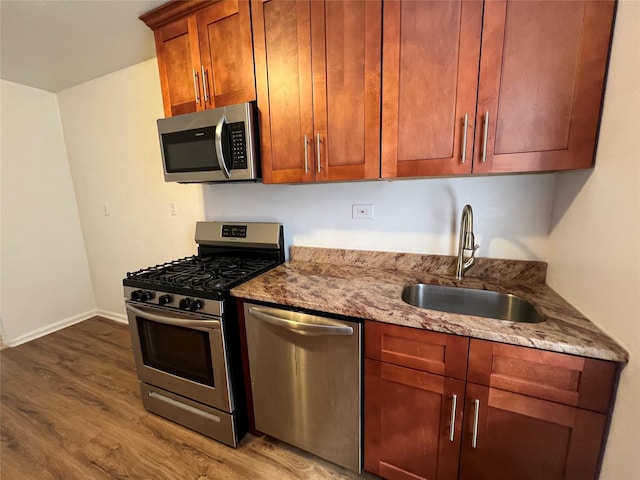 kitchen with hardwood / wood-style flooring, stainless steel appliances, light stone countertops, and sink