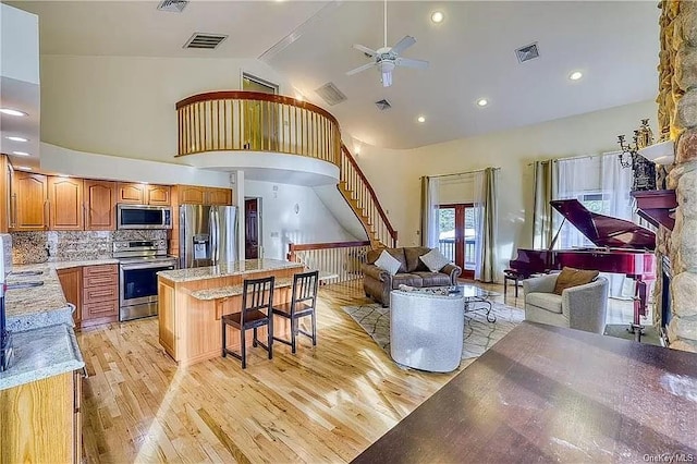 kitchen featuring a kitchen breakfast bar, stainless steel appliances, ceiling fan, high vaulted ceiling, and light hardwood / wood-style flooring