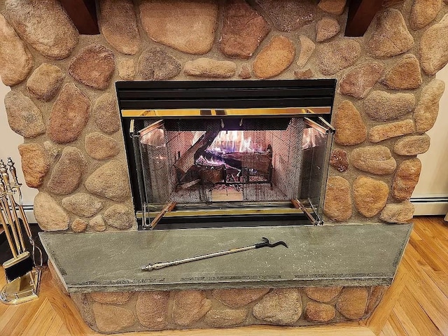 details with a stone fireplace, wood-type flooring, and a baseboard radiator