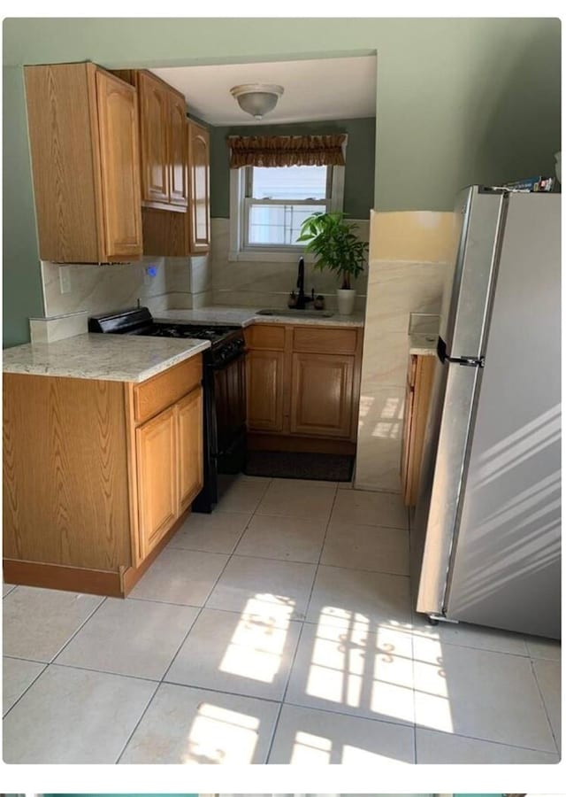 kitchen with backsplash, black range, stainless steel fridge, and sink