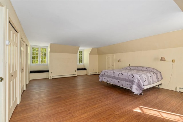 bedroom with lofted ceiling, hardwood / wood-style flooring, and a baseboard heating unit