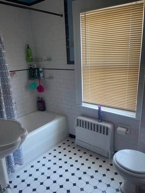 bathroom with radiator heating unit, shower / bath combo, tile walls, and toilet