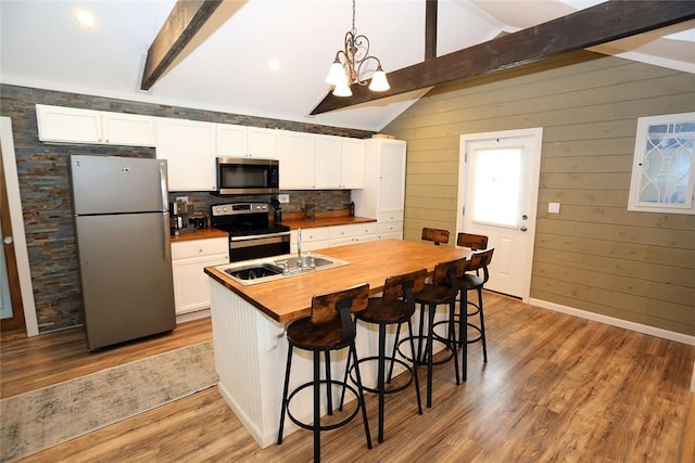 kitchen featuring white cabinets, hardwood / wood-style floors, stainless steel appliances, and wood walls