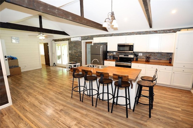 kitchen featuring wood counters, ceiling fan with notable chandelier, stainless steel appliances, decorative light fixtures, and light hardwood / wood-style floors